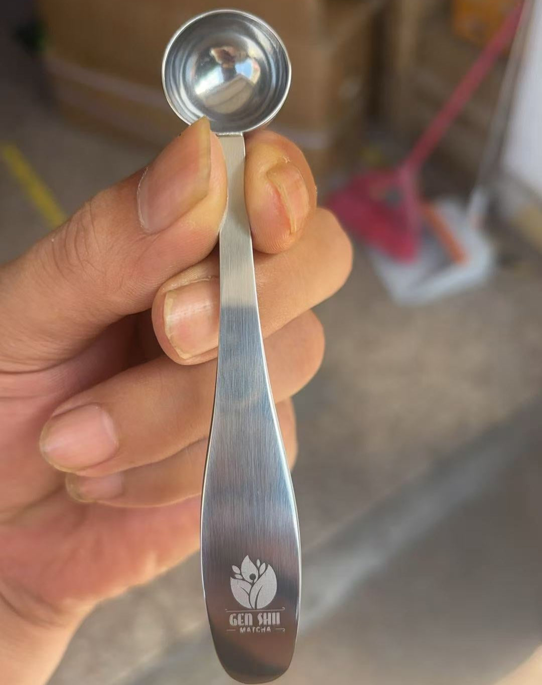 Hand holding a silver measuring spoon with a blurred background